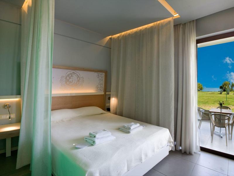 Nowoczesny pokój hotelowy z podwójnym łóżkiem, zasłonami i tarasem z widokiem na krajobraz.