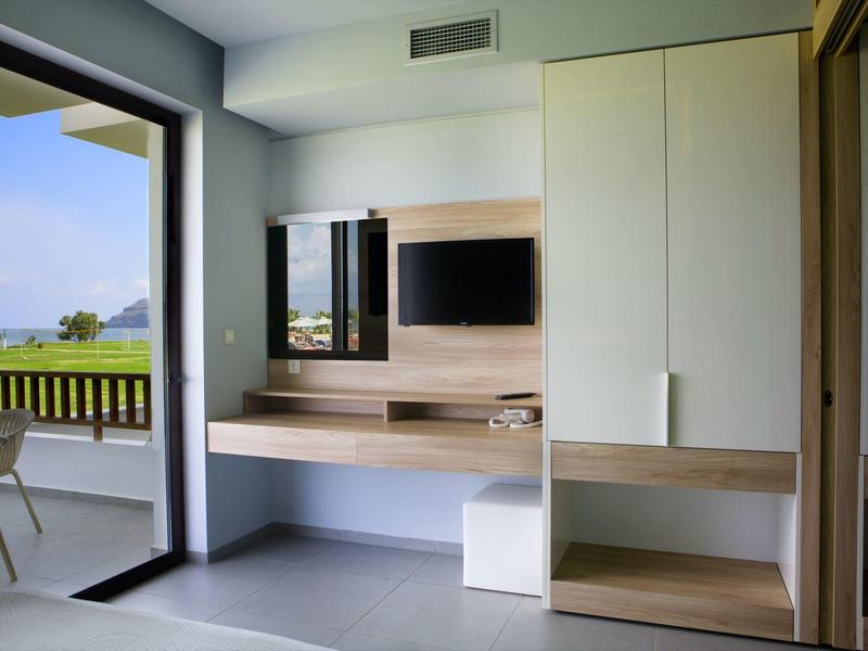 Nowoczesny pokój hotelowy z drewnianymi meblami i balkonem z widokiem na zielony krajobraz.