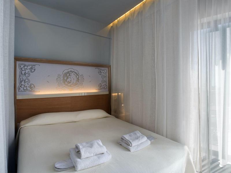 Jasny, nowoczesny pokój hotelowy z podwójnym łóżkiem, świeżymi ręcznikami i dużymi oknami z zasłonami.