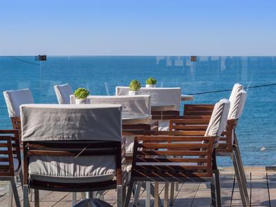 Venku restaurace se stoly a židlemi na terase s výhledem na moře.