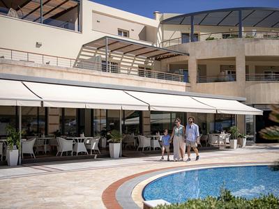 Famille avec enfant marche près de la piscine dans un hôtel ensoleillé avec terrasse extérieure et chaises.