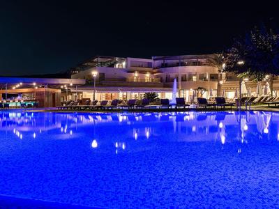 Piscine d'hôtel éclairée avec chaises longues et bâtiment moderne en arrière-plan la nuit.