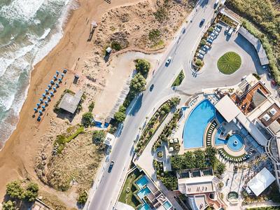 Vue aérienne d'un hôtel avec piscine près d'une plage et d'une route côtière.