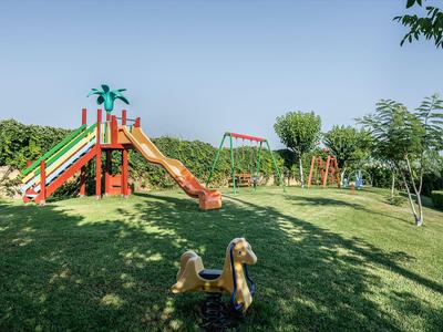 Aire de jeux avec toboggan, balançoires et balançoire sur herbe bien entretenue sous un ciel clair.