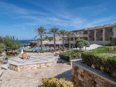 Complexe hôtelier avec piscine, palmiers et vue sur la mer sous un ciel bleu.