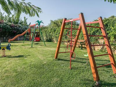 Aire de jeux pour enfants avec structure d'escalade, balançoires et toboggan sur herbe verte.