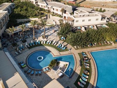 Vue aérienne d'une piscine d'hôtel avec transats, palmiers et bâtiments environnants.