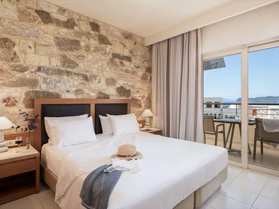 Chambre d'hôtel lumineuse avec lit double, mur en pierre naturelle et balcon vue mer.