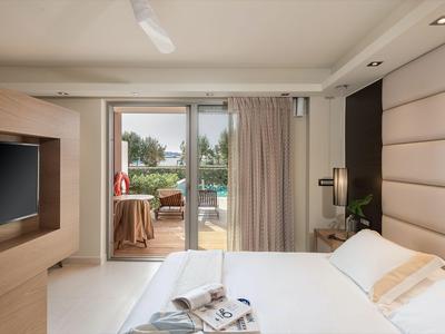 Chambre d'hôtel moderne avec lit, TV et accès à la terrasse et à la piscine.