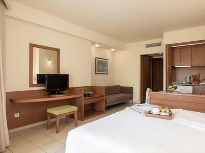Chambre d'hôtel lumineuse avec lit, meubles en bois, téléviseur et petite kitchenette.