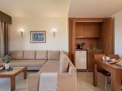 Espace chambre d'hôtel moderne avec canapé beige, meubles en bois et petite kitchenette.