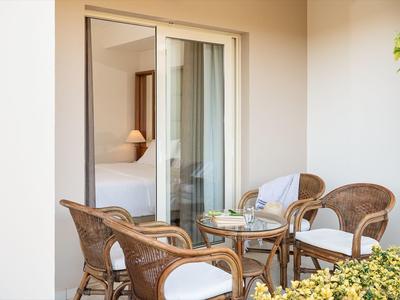 Terrasse confortable avec mobilier en osier et vue sur la chambre d'hôtel avec lit et lampe de lecture.