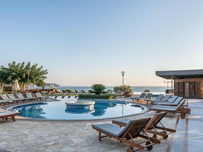 Piscine extérieure ronde avec transats et vue sur la mer sous un ciel dégagé.