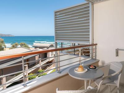 Balcon avec table et chaises donnant sur la mer et des bateaux au loin.