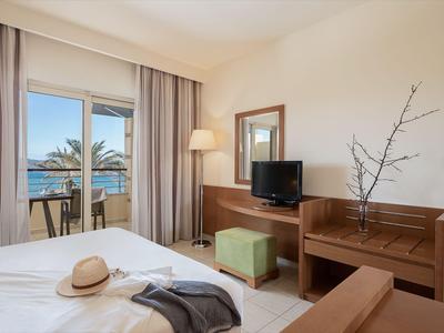Chambre d'hôtel lumineuse avec lit double, télévision, balcon et vue sur la mer.