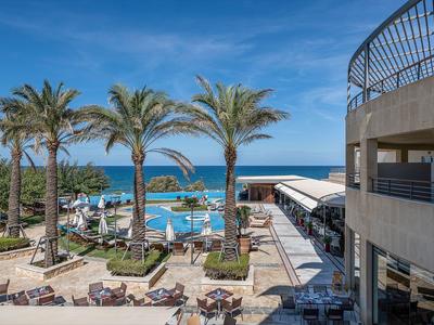 Une zone de piscine d'hôtel avec des palmiers, des chaises longues et vue sur la mer sous un ciel bleu.