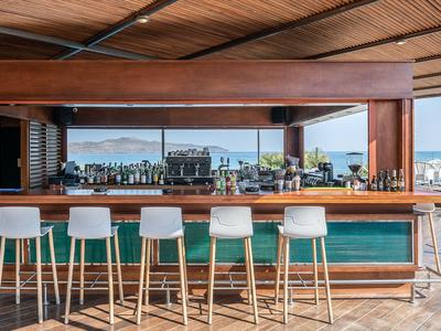 Bar de plage moderne avec plafond en bois et tabourets blancs face à la mer.