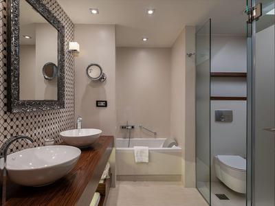 Salle de bains d'hôtel moderne avec plan de travail en bois, deux lavabos, baignoire et douche séparée.