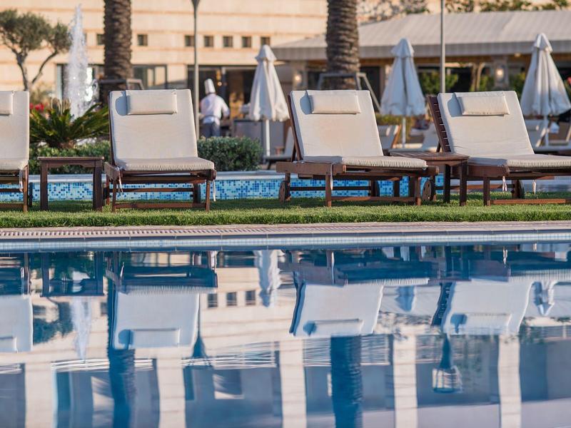 Empty lounge chairs and umbrellas line the edge of a calm hotel pool.