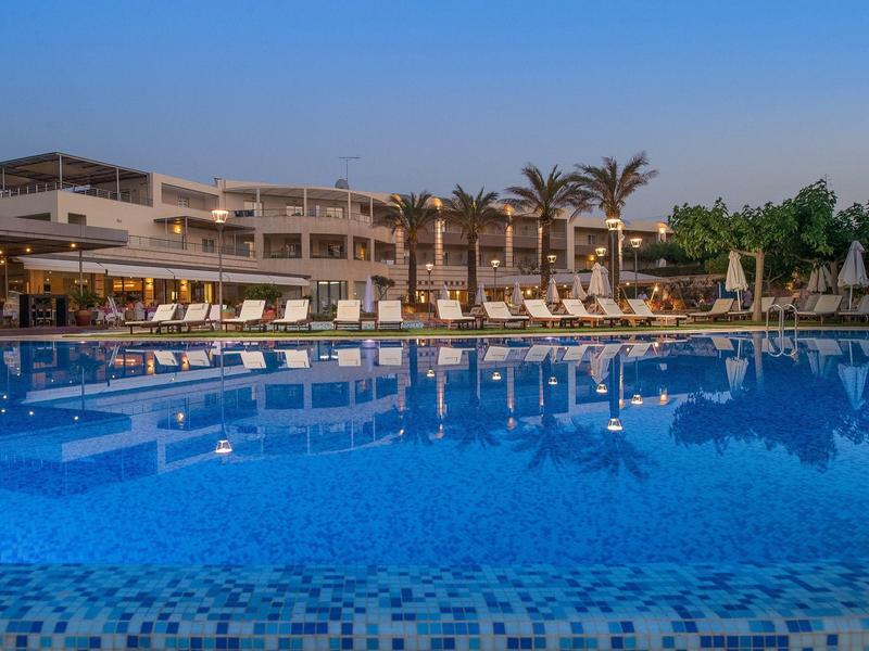 A calm hotel pool with sun loungers and palm trees at sunset.