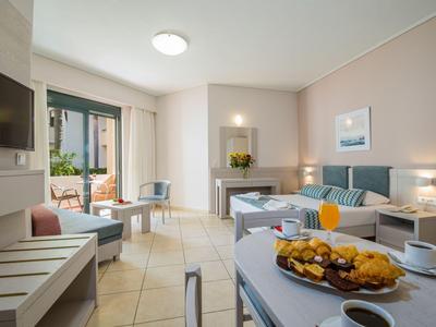 Helle Hotelzimmer mit Sitzbereich, Balkon und gedecktem Frühstückstisch.