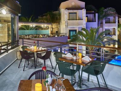 Terrace with tables and chairs next to a lit pool in a hotel complex at night.