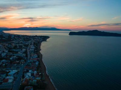 Aerial view of a coastal town at sunset with calm sea and island on the horizon.