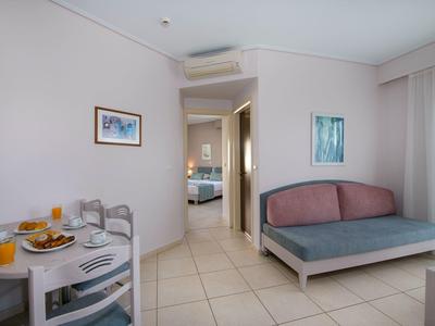 Bright hotel room with table, chairs, sofa, and view into bedroom.