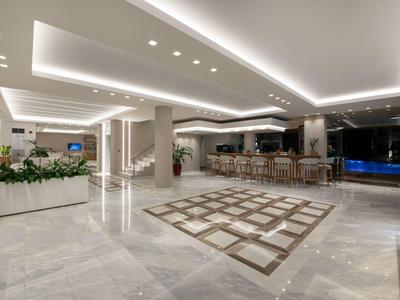 Světlá hotelová lobby s elegantní mramorovou podlahou, barem a moderním osvětlením.