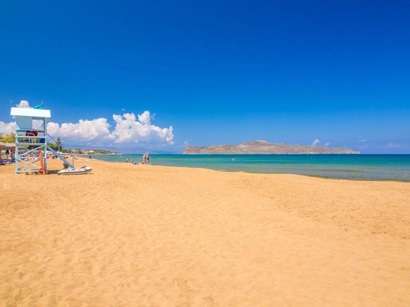 Wide, calm sandy beach with clear sky and a lifeguard tower on the shore.