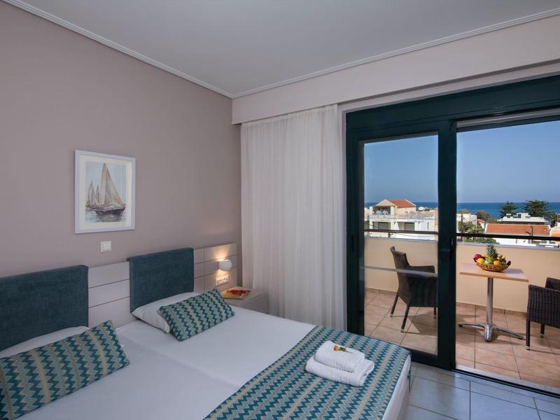 Modern hotel room with double bed and balcony overlooking the sea.