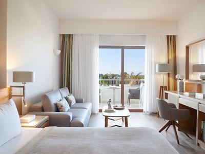 Moderní hotelový pokoj s postelí, sedací částí a balkonem s výhledem na moře.