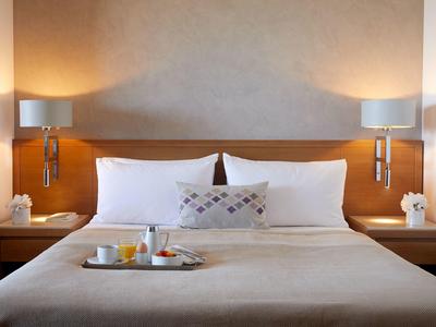 Pohodlná hotelová postel s bílými polštáři, nočními lampami a tácem na snídani.