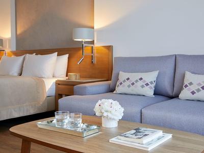 Moderní hotelový pokoj s postelí, pohovkou, dřevěným stolem, lampou a květinovou dekorací.