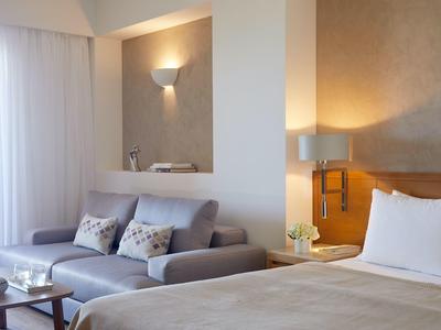 Moderní hotelový pokoj s postelí, pohovkou, stolem a jemným osvětlením.