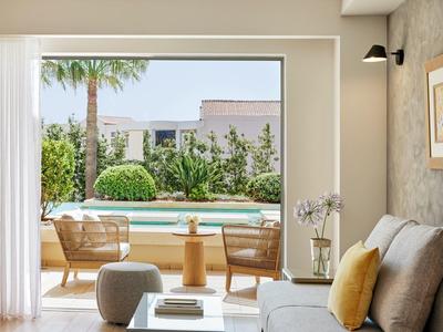 Moderní obývací prostor s pohovkou, křesly a výhledem na zahradu s bazénem a palmami.