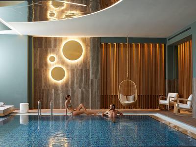 Vnitřní bazén s moderním kulatým osvětlením, dvě osoby ve vodě a závěsná židle.