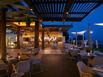 Pohodlné venkovní posezení v restauraci pod pergolou s večerním osvětlením u moře.