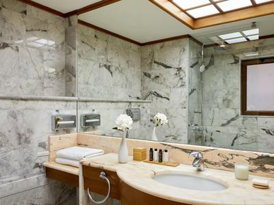 Moderní interiér koupelny s mramorovými zdmi, velkým zrcadlem a dřevěnou umyvadlovou skříňkou.