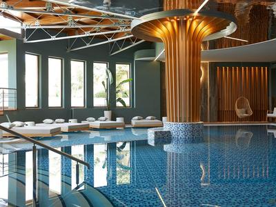 Vnitřní bazén s modrými dlaždicemi, dřevěným sloupem, lehátky a velkými okny s přirozeným světlem.