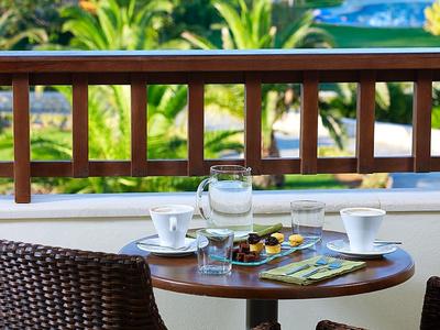 Stůl s nápoji a pochutinami na terase s výhledem na bazén a tropické rostliny.