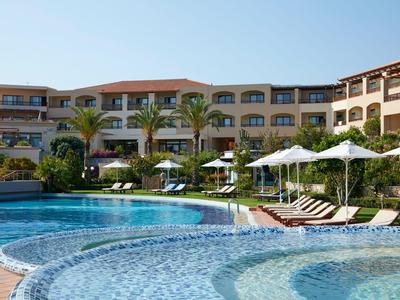 Großer Hotelpool mit Liegestühlen und Sonnenschirmen vor einem mehrstöckigen Hotelgebäude.