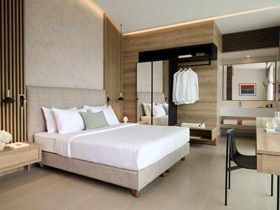 Moderní hotelový pokoj s velkou postelí, pracovním stolem a otevřenou skříní v neutrálních barvách.