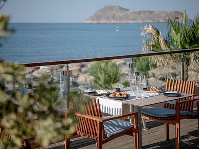 Terrasse de restaurant avec tables et chaises en bois avec vue sur la mer et une île à l'arrière-plan.