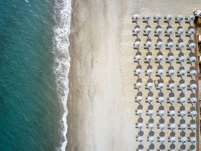 Vue aérienne d’une plage avec des vagues et des rangées de parasols et de chaises longues près d’un hôtel.