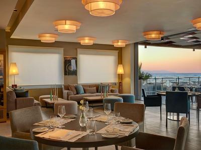Restaurant moderne avec tables dressées et vue sur le coucher de soleil en mer.