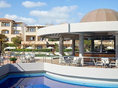Terrasse d'hôtel avec espaces assis, piscine et parasols sous un ciel bleu.