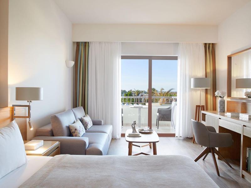 Moderní hotelový pokoj s postelí, sedací částí a balkonem s výhledem na moře.
