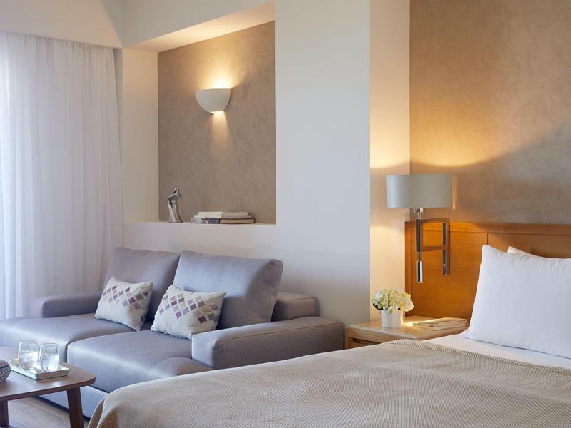 Moderní hotelový pokoj s postelí, pohovkou, stolem a jemným osvětlením.