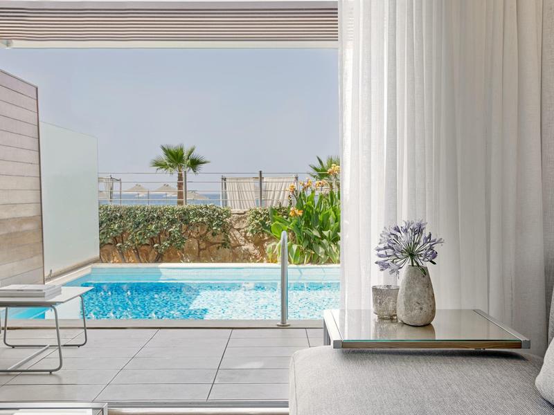 Moderní lounge prostor s výhledem na bazén a zahradu za denního světla.